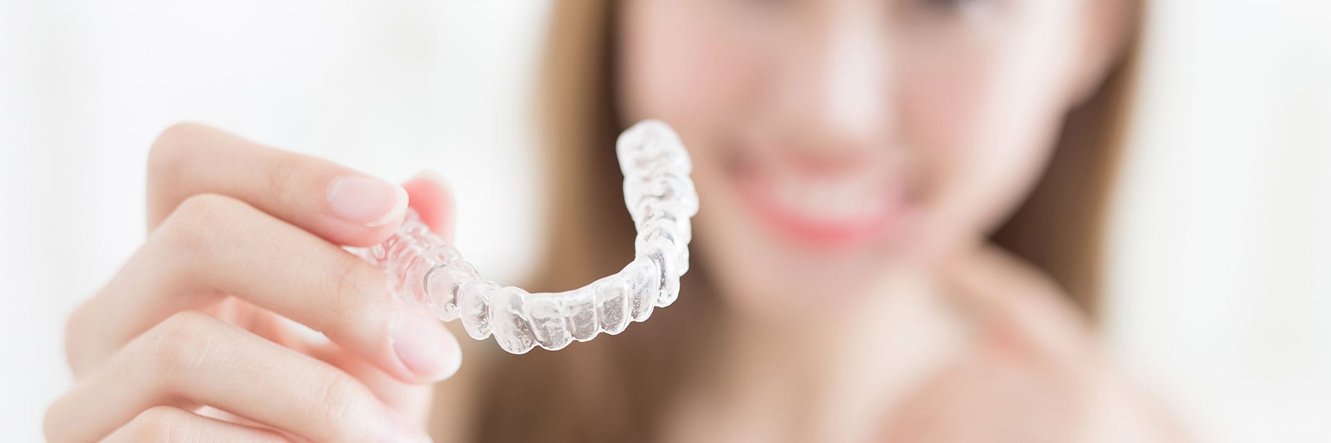 Nasmijana žena drži nevidljivi Invisalign aparatić