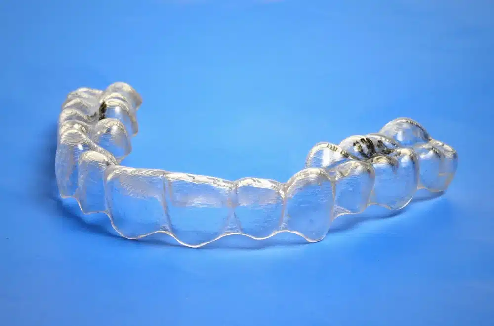 Jedan prozirni Invisalign aparatić položen na svijetloplavoj podlozi.